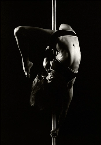 Pole dancer hanging upside down with her mid-section exposed.